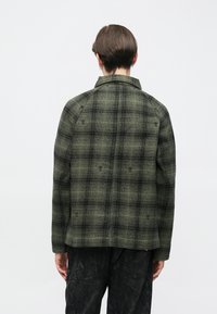 Zielono-czarna kurtka w kratę wykonana z teksturowanej tkaniny, charakteryzująca się prostokątnym krojem, tylną karczkiem oraz subtelnymi haftowanymi detalami.