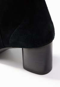 Bottine en daim noir avec bout arrondi, dessus texturé et talon cylindrique épais à surface striée.