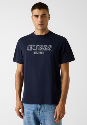 Marineblauw katoenen T-shirt met het "GUESS"-logo en "EST. 1981" in contrasterende stiknaden. Korte mouwen, ronde hals, losse pasvorm.