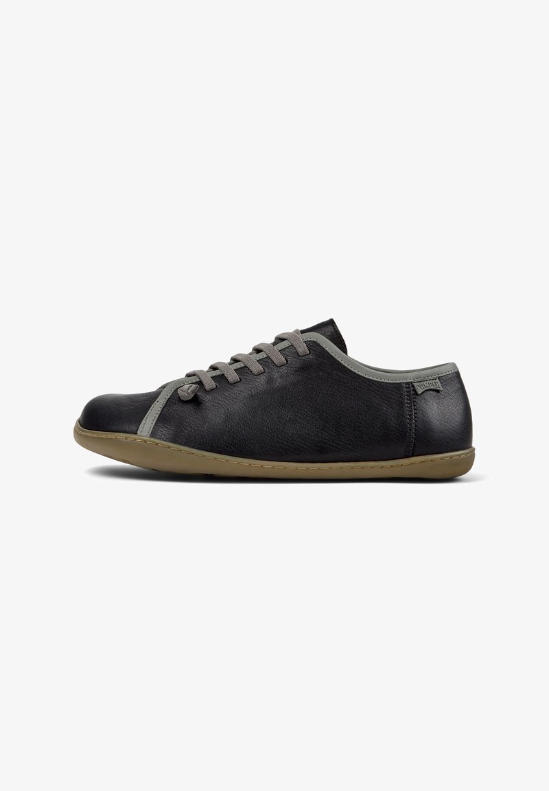 Scarpe in pelle nera con accenti grigi, caratterizzate da un profilo basso e un design con lacci, esposte su uno sfondo bianco.