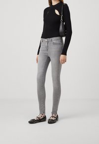 Top de manga larga negro con relieve y cortes, jeans skinny grises y bailarinas negras con lunares y detalle de lazo. Pequeño bolso negro.
