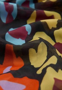 Gros plan sur un tissu texturé aux motifs floraux abstraits en rouge, jaune, bleu, orange et noir.