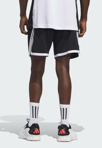 Pantalones cortos deportivos negros con ribete blanco, franjas laterales y un ajuste holgado, combinados con calcetas blancas con rayas negras y zapatillas deportivas negras.