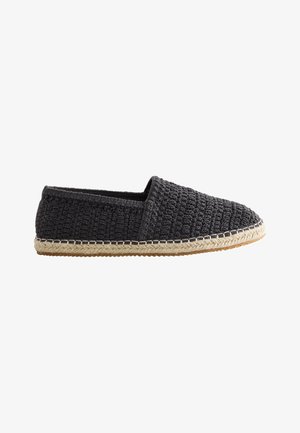 Melns austs slip-on espadrils ar jūtas apjoztu zolīti un gumijas apakšu, attēlots uz baltas fona.