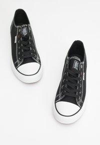 Sneakers neri in tela con punte e suole in gomma bianca, dotati di lacci neri, cuciture a contrasto e logo sulla linguetta.