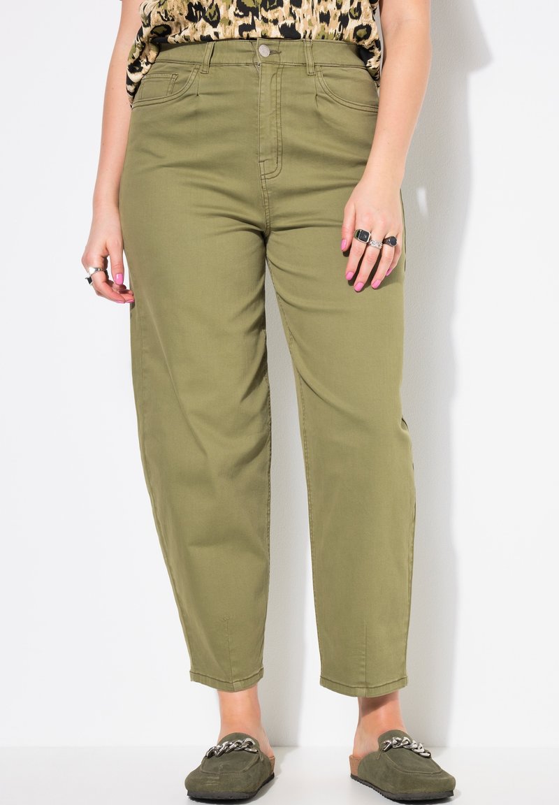 Pantalones cargo de algodón verdes con cintura alta, piernas rectas y bolsillos frontales, combinados con zapatos de entrada marrones y anillos en las manos.