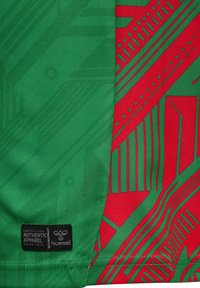 Groene sportshirt met een rood geometrisch patroon, textuurstof en een zwart merklabel aan de zoom. Kenmerkende design elementen en kleuren.