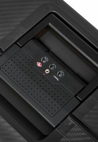 Zwarte koffer met TSA-combinatieslot met drie dials en een sleutelgat, geïntegreerd in het gestructureerde oppervlak en de handgreep van de koffer.