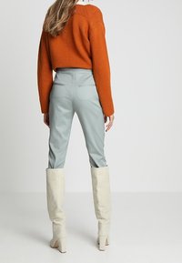 Světlé modré kalhoty na míru spárované s oranžovým krátkým svetrem. Kalhoty mají hladkou texturu a zadní kapsy; svetr má žebrovaný výstřih.