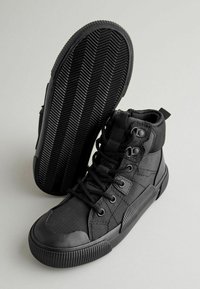 Schwarze High-Top-Schuhe aus Canvas und Gummi, mit einer strukturierten Oberfläche, runden Schnürsenkeln und einer gemusterten Sohle mit Fischgrät-Rillen.
