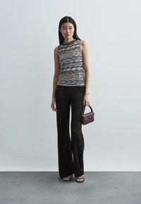 Top senza maniche in maglia con motivo a onde in nero, bianco e arancione, abbinato a pantaloni svasati marrone scuro e borsa bordeaux.