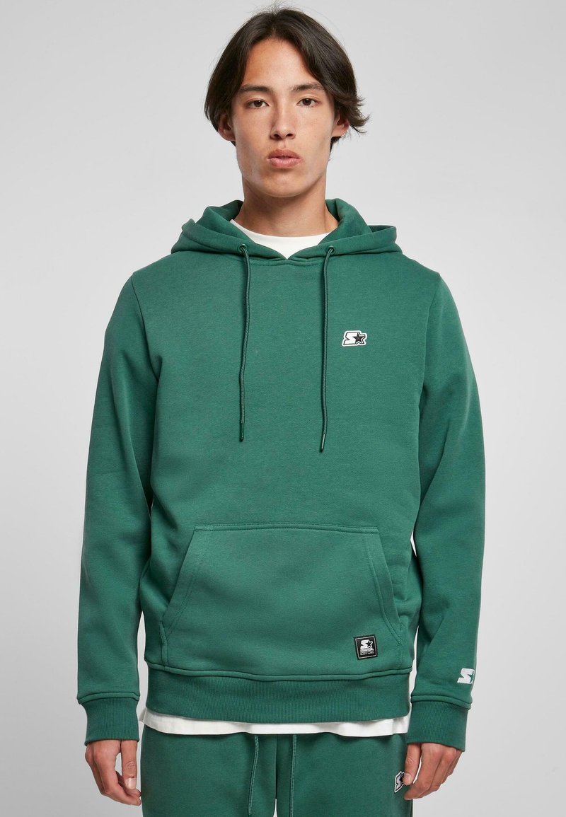 Sudadera verde hecha de tela suave, con un bolsillo frontal tipo canguro, capucha ajustable con cordones, logo en el pecho y puños acanalados.