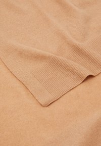 Pull en cachemire pêche doux avec poignets côtelés, présentant une texture lisse et un design sans coutures, mettant en avant la chaleur et le confort.