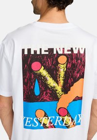 White cotton t-shirt featuring a colorful graphic on the back. Design includes bold lines, various shapes, and text in contrasting colors.