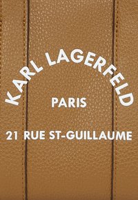 Cuir texturé marron avec du texte en relief blanc : "KARL LAGERFELD PARIS 21 RUE ST-GUILLAUME," présentant des accents de couture horizontaux.