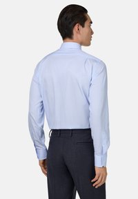 Lichtblauw gestreepte overhemddress met een spread collar, knoopmanchetten en een gladde textuur, gedragen met donkere, op maat gemaakte broek.