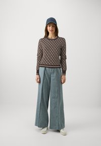 Brown patterned sweater with ribbed cuffs, paired with wide-legged light blue denim trousers and white sneakers. Blue cap completes the outfit.