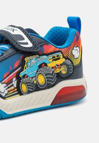 Blue and black sneaker with a textured upper, featuring a monster truck graphic and colorful design accents. Velcro strap for closure.