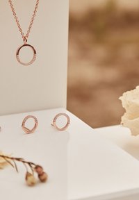 Set di gioielli in oro rosa composto da una collana con pendente circolare decorato con accenti in cristallo e orecchini a bottone circolari coordinati. Finitura liscia e lucida.