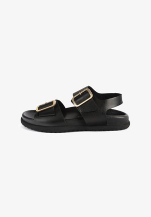 Zwarte leren sandalen met twee brede banden en gouden rechte gespen, een platte zool en een getextureerde voetbed voor comfort.