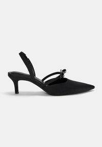 Svart spetsig tå slingback-klack med tunna remmar och en dekorerande rosett. Tillverkad av slätt material och har en klack på 5 cm för ökad höjd.