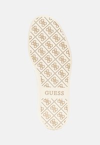 Baldai balti guminių batų padai, su raštuota interlocking logotipų dizainu, sudarytu iš rombų tinklo su prekės ženklu "GUESS" iškaltu.