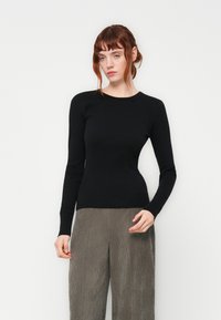 Black long-sleeve ribbed top with a round neckline, fitted silhouette, and seamless cuffs, paired with textured grey wide-leg pants.