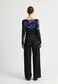 Langärmliges schwarzes Oberteil mit blauem Blumenmuster, kombiniert mit hochtaillierten, weiten schwarzen Jeans. Glatte Textur und figurschmeichelnder Schnitt.