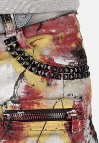 Shorts en denim avec un motif éclaboussé de peinture multicolore en rouge, jaune et noir. Dotés d'éclats métalliques et d'une poche zippée.