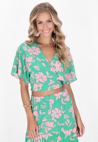 Top corto verde floreale con motivo di fiori rosa, maniche ampie e scollatura a V, abbinato a una gonna elastica in vita dello stesso tessuto.