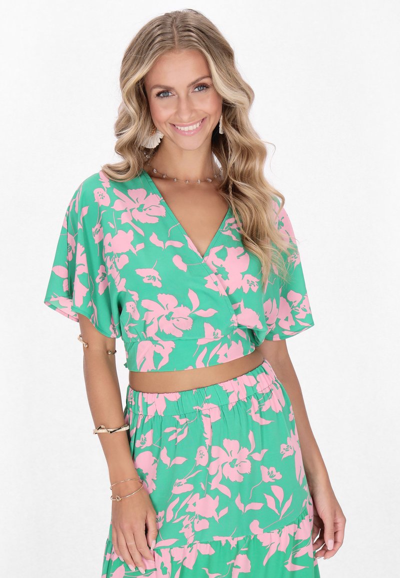 Top corto verde floreale con motivo di fiori rosa, maniche ampie e scollatura a V, abbinato a una gonna elastica in vita dello stesso tessuto.