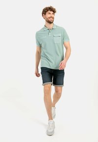 Lichtgroen polo shirt met een borstzak, met een eenvoudig ontwerp. Gecombineerd met opgerolde denim shorts en witte sneakers.