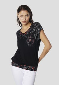 Schwarzes V-Ausschnitt-Top mit kurzen Ärmeln, verziert mit roten und weißen Blumenmustern entlang des Ausschnitts und Saums, aus weichem Stoff gefertigt.