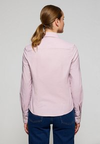 Camicia button-up rosa chiaro con maniche lunghe, taglio aderente e motivo a quadretti discreto. Presenta un colletto classico e polsini con bottoni.