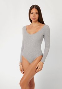 Bodysuit a maniche lunghe in tessuto a coste grigio chiaro. Presenta una profonda scollatura a V e gambe alte per una silhouette aderente.