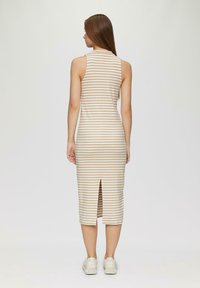 Gestreiftes Midikleid in Beige und Creme, ärmellos mit einem Schlitz hinten, figurbetontes Design. Getragen mit weißen Sneakers. Glatte Textur.