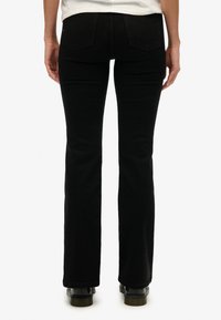 Jeans negros de corte acampanado fabricados en denim. Presentan una textura suave, diseño de cinco bolsillos y bolsillos traseros con solapas apuntadas.