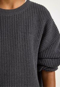 Sweter w kolorze węglowym, dziany, z teksturowanym wzorem, szerokimi mankietami i okrągłym dekoltem. Materiał wydaje się miękki i gruby.