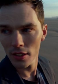 Nahaufnahme einer Person mit heller Haut, kurzen dunklen Haaren, die eine schwarze Jacke trägt. Der Hintergrund ist verschwommen und hebt die Gesichtszüge und den Ausdruck hervor.