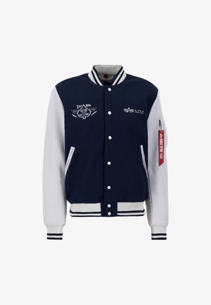 Námornícka a biela varsity bunda s vlněným telom, rebrovanými manžetami, zacvakávacím zapínaním, vyšívanými nášivkami a štítkom na ľavom rukáve.
