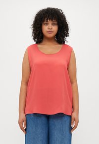 Coral sleeveless top with a rounded neckline, made of smooth fabric. Paired with blue wide-leg jeans. Simple, clean design with no patterns.
