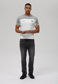 Gray and white short-sleeve T-shirt with a round neck, featuring a logo and contrast stitching. Paired with black jeans and sneakers.