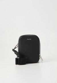Black Calvin Klein crossbody bag with silver zipper and adjustable fabric strap on a white background.