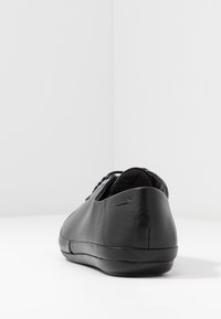 Čierne kožené tenisky s hladkým povrchom, zaoblenou špičkou, kontrastnými šnúrkami a nenápadným logom na päte. Minimalistický dizajn.