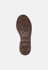 Suola di scarpa in gomma marrone con motivo testurizzato, caratterizzata da scanalature e linee. Nome del marchio "Camper" e taglia "38" visibili sulla suola.