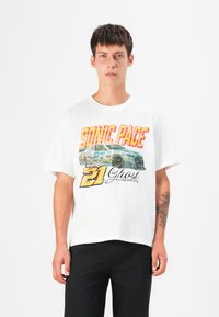T-shirt en coton blanc avec un imprimé graphique color�é portant le texte "SONIC PACE" et un design de voiture de course. Coupe décontractée, col rond.