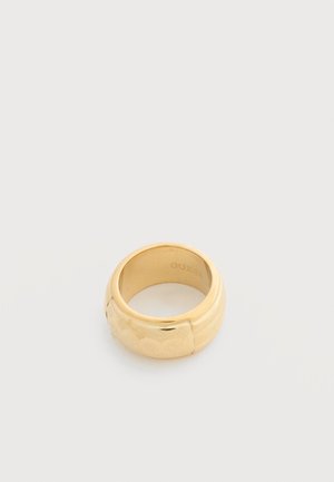 Bague jonc en métal doré avec motifs floraux et logo gravés, design large et arrondi, présentée sur un fond gris clair.