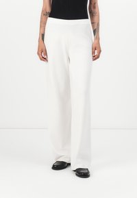 Wijdvallende, witte gebreide broek met een gestructureerde afwerking en een elastische tailleband, gecombineerd met zwarte schoenen. Kenmerkt een lange, rechte silhouet.