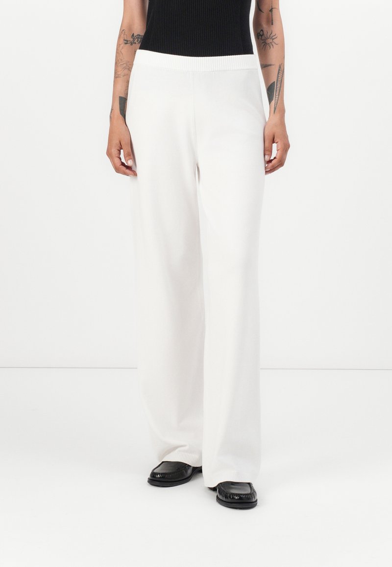 Wijdvallende, witte gebreide broek met een gestructureerde afwerking en een elastische tailleband, gecombineerd met zwarte schoenen. Kenmerkt een lange, rechte silhouet.