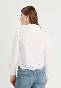 Chemise blanche à manches longues avec un col et de la broderie œillets à l'ourlet. Assortie à un bas en denim bleu clair.